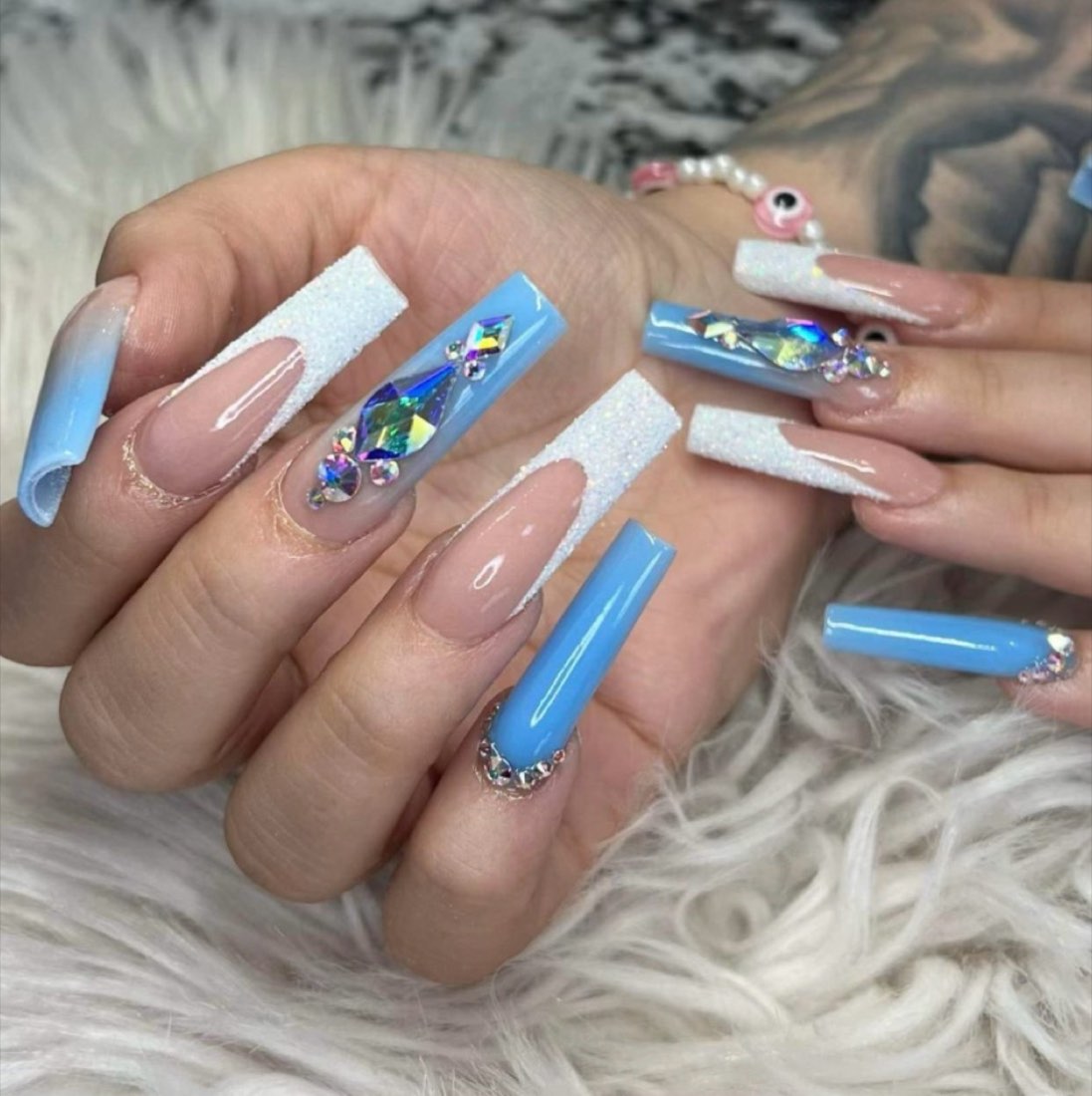 Long blue coffin nails with a large center crystal and white glitter french accent nails