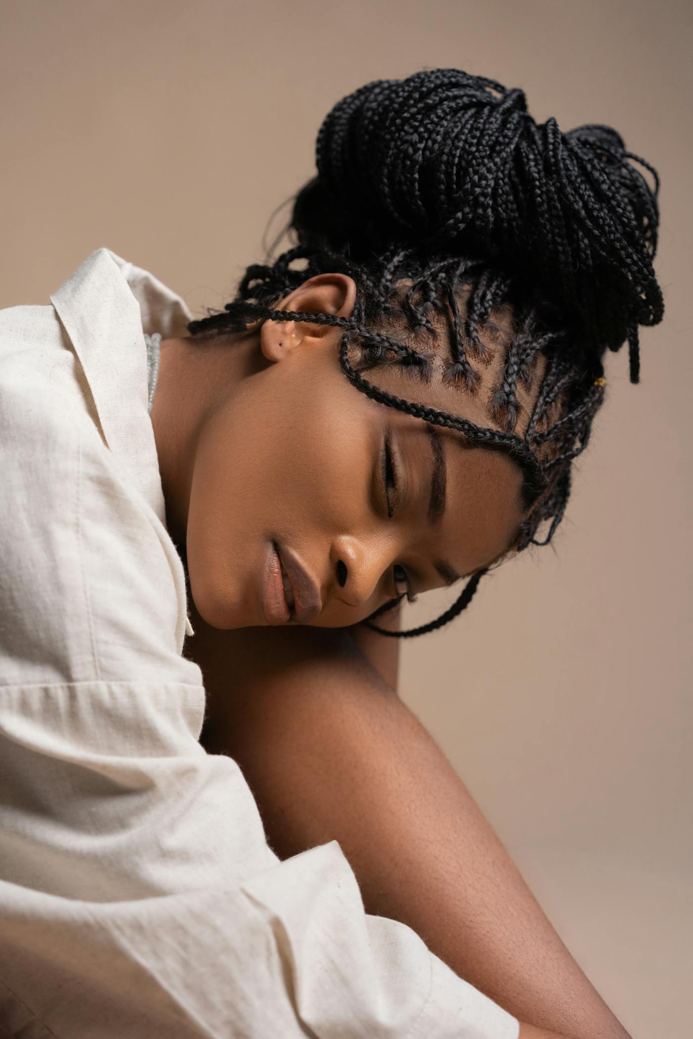 Box braids styled into a soft bun against a warm bone-toned studio backdrop