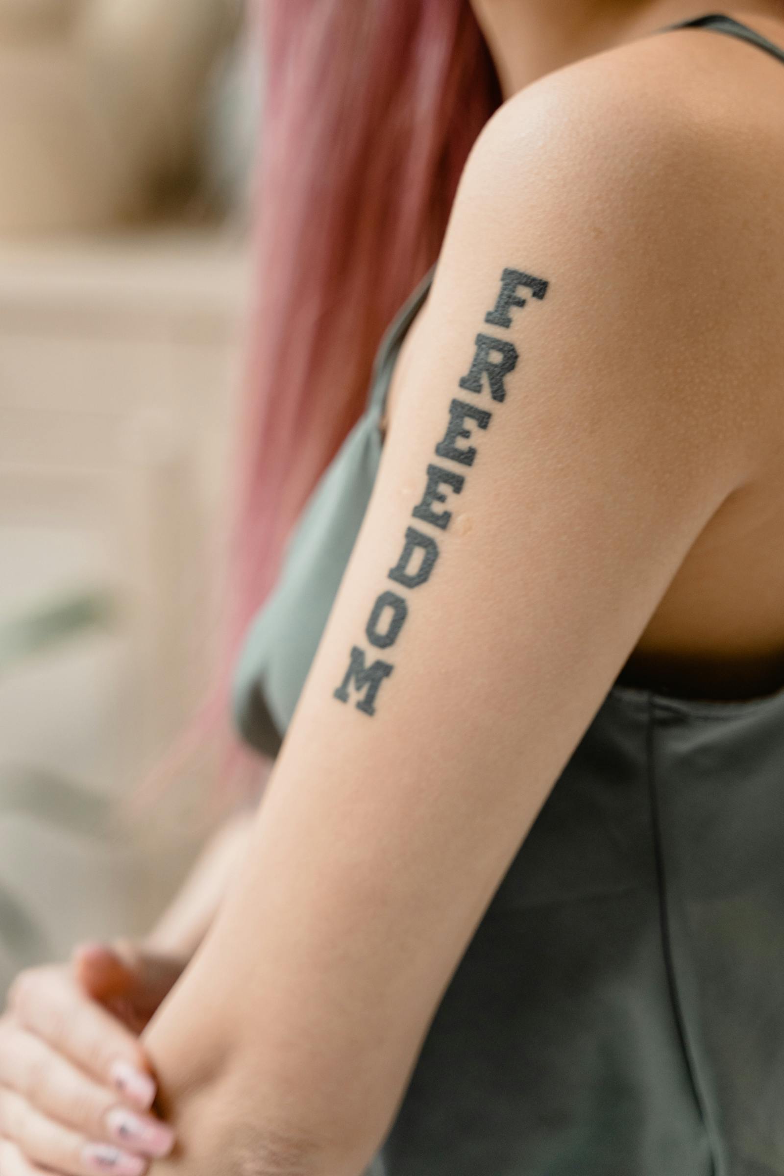 Bold vertical lettering tattoo reading 'Freedom' down an upper arm