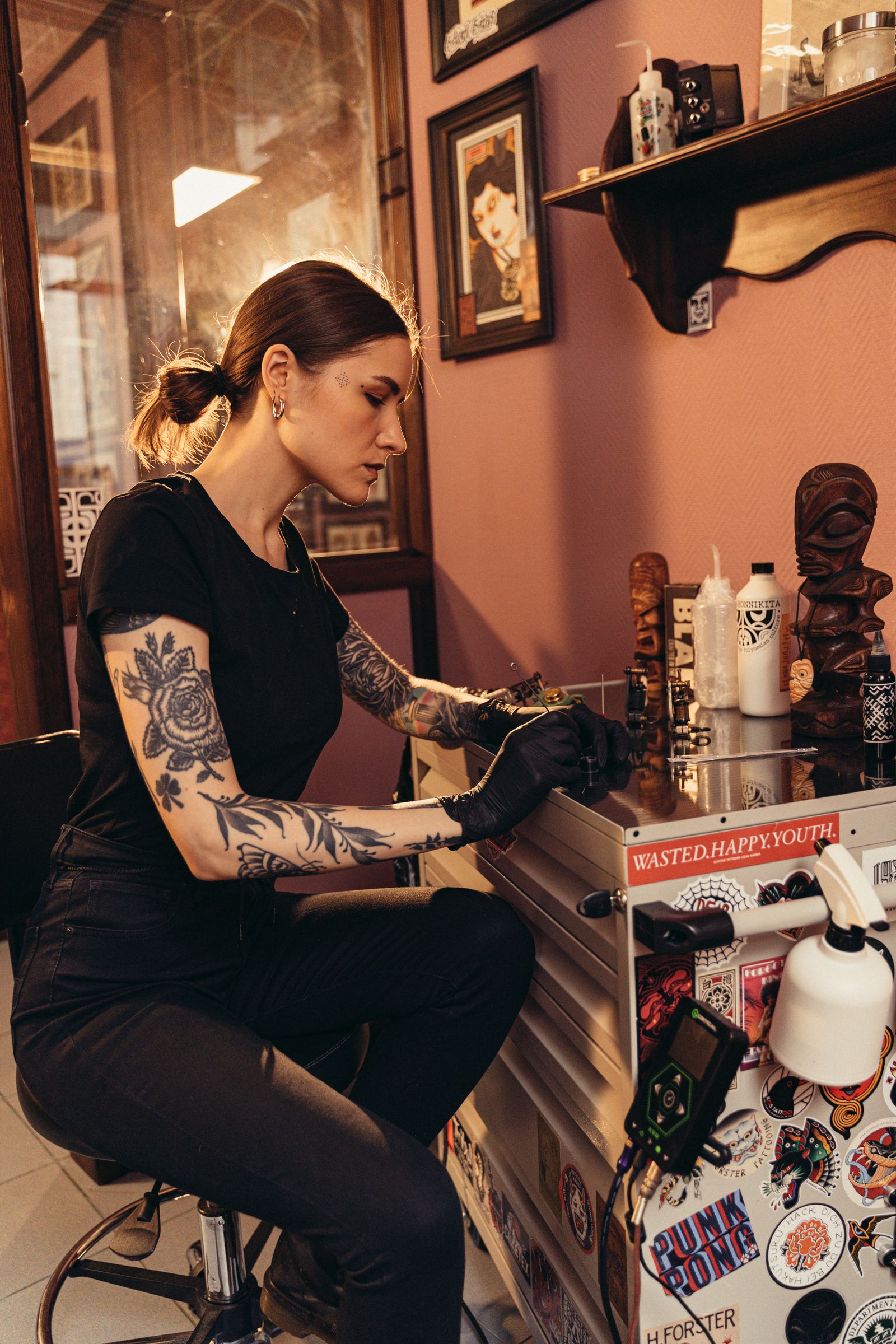 Tattoo artist working at a warm, character-filled station in a neighborhood shop