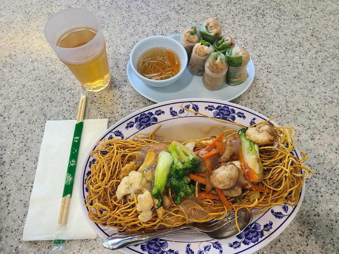 Stir-fried noodles with broccoli, carrot and soy chicken on a blue-and-white plate, with tea